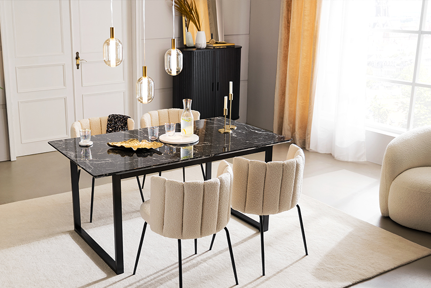 Eleganter Essbereich im Glamourstil mit eleganten Stühlen in beigem Boucléstoff und einem Tisch in Marmoroptik, darauf goldene Schalen, ein Marmortablett und Gläser mit Goldrand, im Hintergrund schwarze Stauraummöbel mit edlen Lamellenfronten.