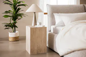 Lit capitonné beige Retreat, table basse Baliza en travertin et lampe gris clair.