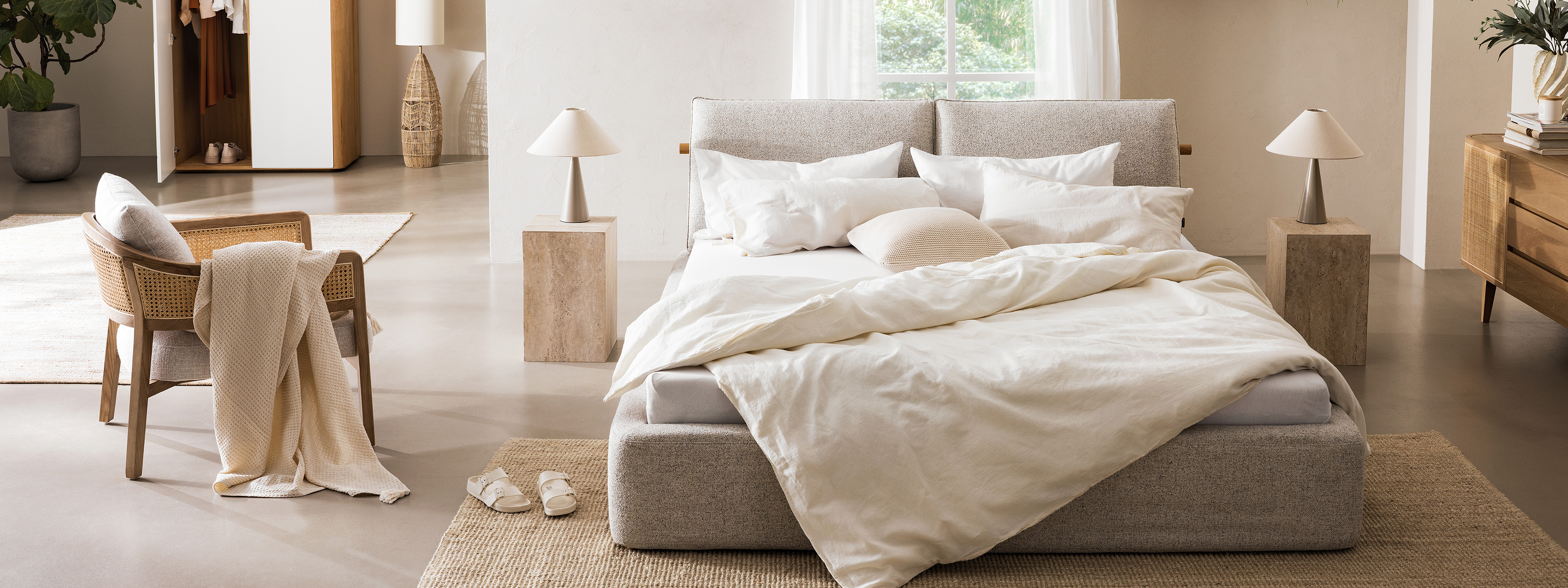 Chambre dans un style bohème avec le lit capitonné beige Retreat de chez home24, du rotin, des textiles et des plantes.