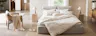 Chambre dans un style bohème avec le lit capitonné beige Retreat de chez home24, du rotin, des textiles et des plantes.