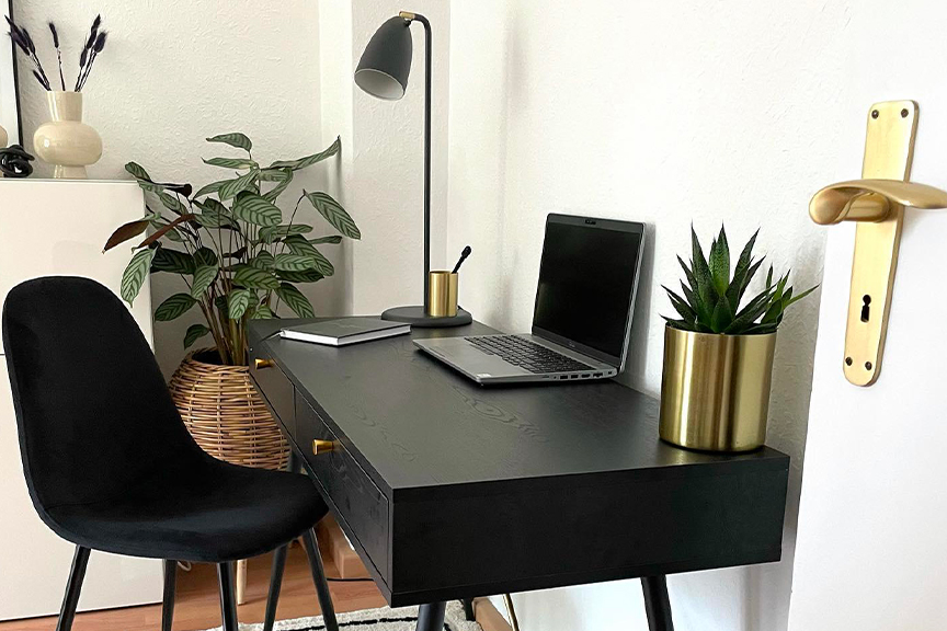 Schwarzer Schreibtisch von home24, der mit goldenen und schwarzen Accessoires gestylt ist