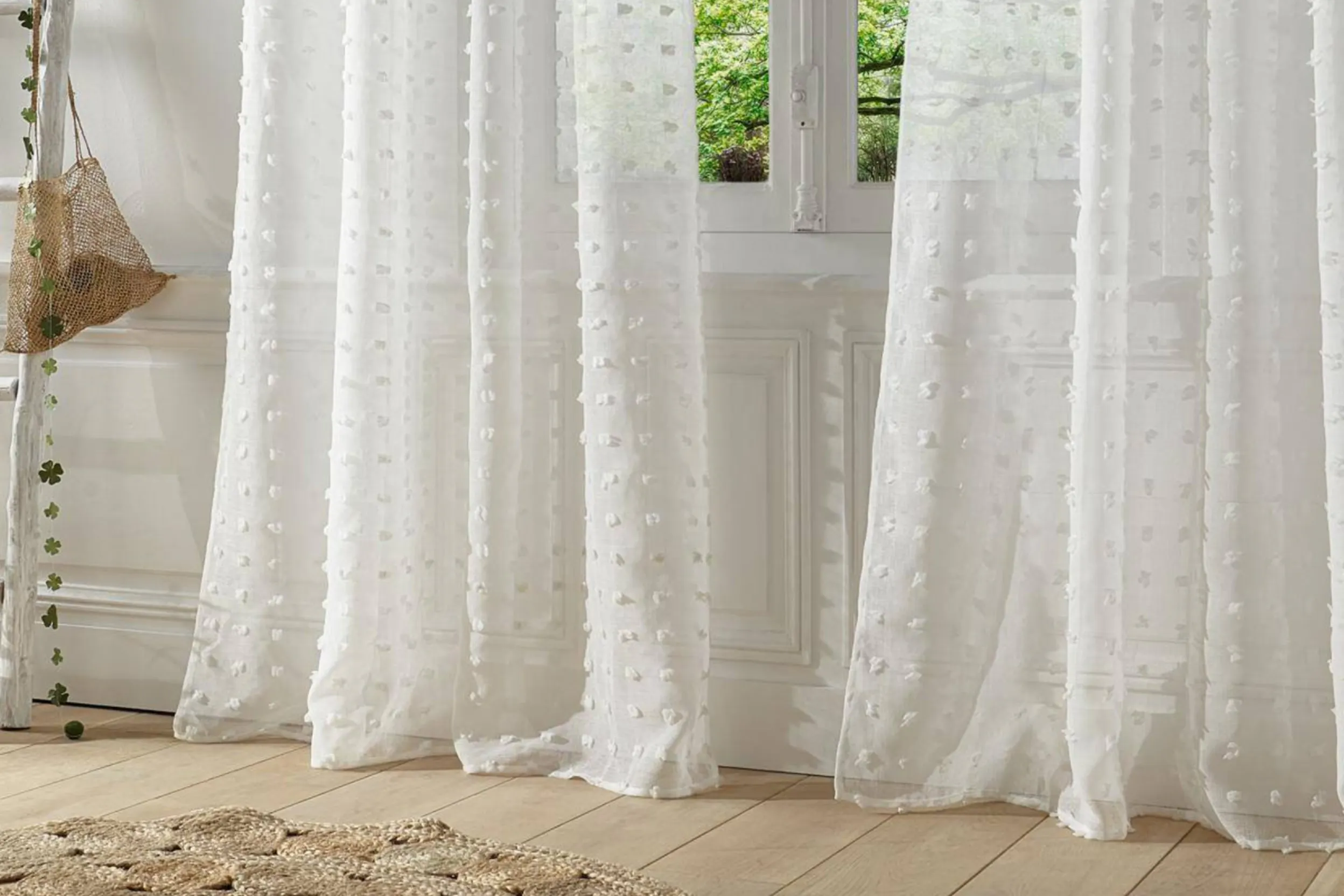 Transparente weiße Vorhänge mit Punkten hängen vor einem Fenster