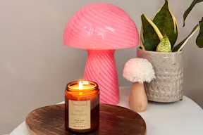 Mehrere bunte Tischlampen in Pilzform auf einem dunkelgrünen Sideboard vor pinkfarbener Wand.