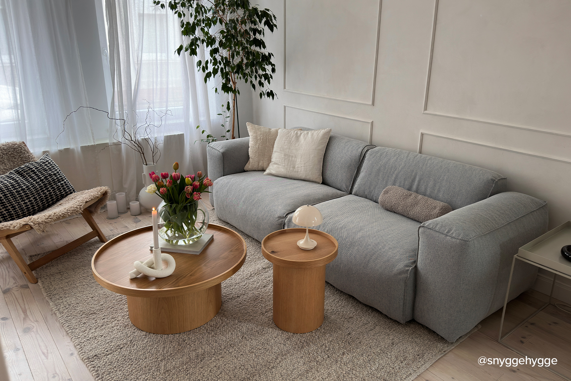 Wohnzimmer mit grauem Sofa, einem Sessel im Retro-Look sowie runden Couchtischen aus Holz im Naturstil.