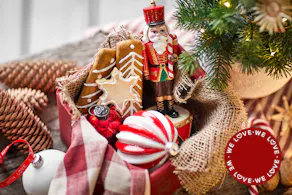 Des décorations de Noël traditionnelles comme des boules rouges, des pendentifs en forme de biscuits et un casse-noisette rouge ; à côté, une table dressée de manière classique avec du sapin, des touches de rouge et des couverts dorés.