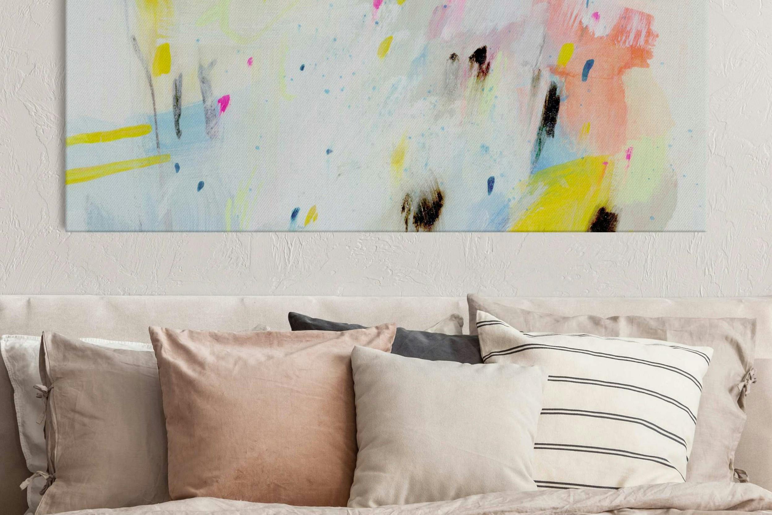 Verschiedene Dekokissen vor einer Wand mit einem farbenfrohen Akustikbild