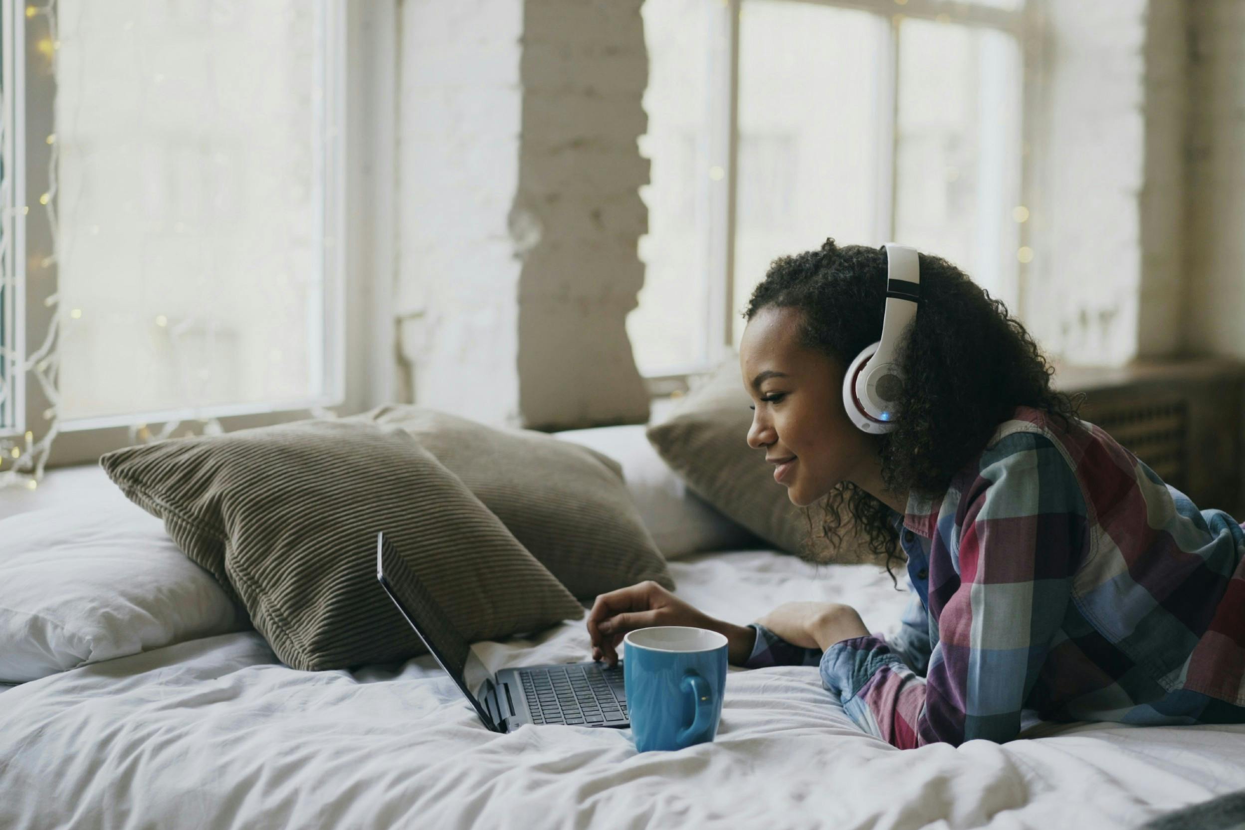 Junge Frau mit Noise-Cancelling-Kopfhörern und Laptop auf dem Bett