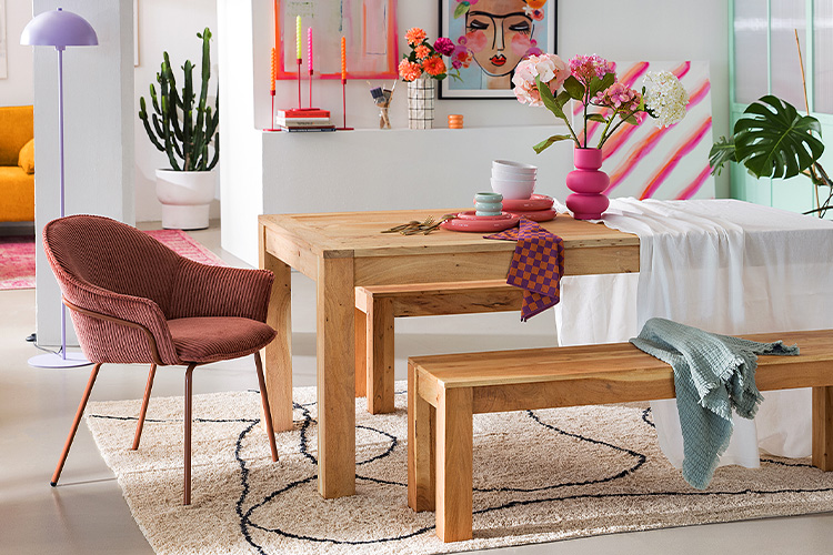 Esstisch aus Massivholz mit bunter Boho-Tischdeko in Pink, Orange und Türkis; dazu farblich passende Polsterstühle.