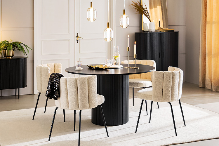 Schwarzer, runder Esstisch mit eleganter Tischdeko und Lampen in Gold sowie beigen Polsterstühlen.