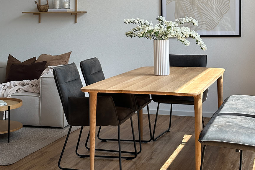 Topseller Esstisch Fleek aus hellem Massivholz im schlanken Skandi-Design in Kombination mit schwarzen Polsterstühlen und Pendelleuchten.