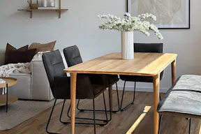 Topseller Esstisch Fleek aus hellem Massivholz im schlanken Skandi-Design in Kombination mit schwarzen Polsterstühlen und Pendelleuchten.