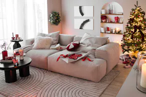 Salon décoré pour Noël avec un grand canapé lounge comme pièce maîtresse de la pièce, accompagné de décorations ludiques en rouge et rose avec de jolis motifs de bonbons.