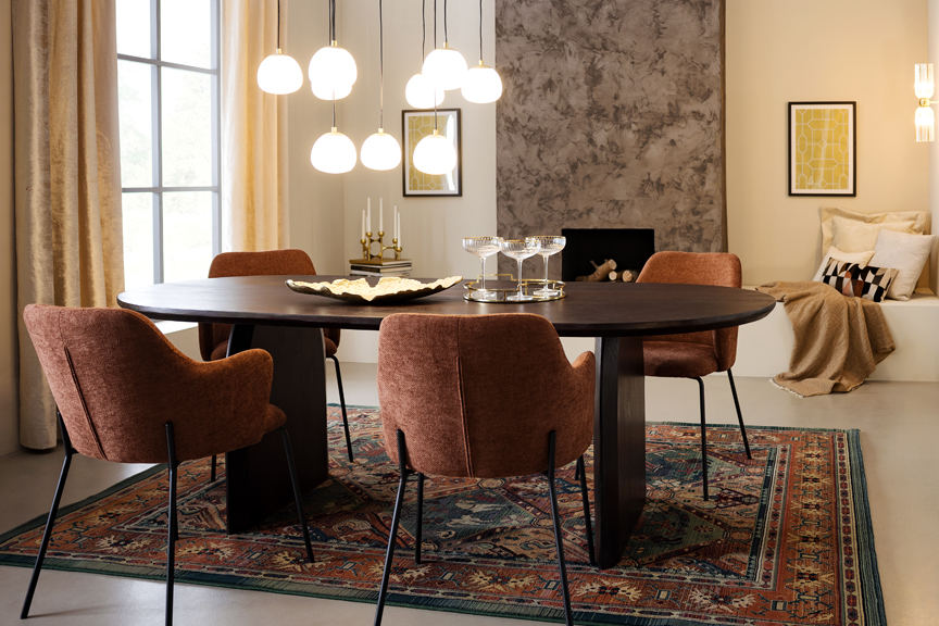 Esszimmer im modernen Art-déco-Stil mit einem schwarzen Esstisch, braunen Polsterstühlen, goldfarbenen Pendelleuchten in Kugelform, einem schwarzen Sideboard sowie einem gemusterten Teppich.