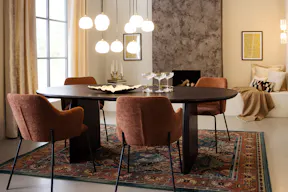 Esszimmer im modernen Art-déco-Stil mit einem schwarzen Esstisch, braunen Polsterstühlen, goldfarbenen Pendelleuchten in Kugelform, einem schwarzen Sideboard sowie einem gemusterten Teppich.