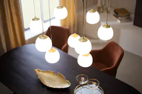 Über einem schwarzen Esstisch hängen messingfarbene Kugellampen im Art-déco-Stil.