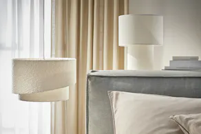 Suspension beige-blanc en bouclé et lampe de table blanche en tissu, accompagnées du lit boxspring KINX en gris.