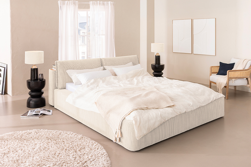 Minimalistisch eingerichtetes Schlafzimmer mit einem weißen Bett in voluminösem, cremeweißem Cordstoff und vielen luftigen Textilien; daneben ein Bild von einem Himmel mit weißen Wölkchen.