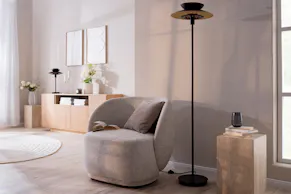 Dunkelgrauer Sessel mit einer schwarzen Stehlampe in einem Schlafzimmer, das hauptsächlich in warmen Grau- und Erdtönen eingerichtet ist.