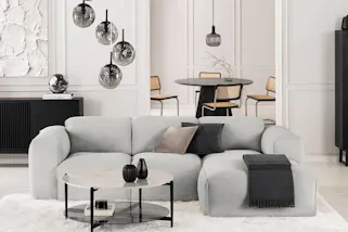Modern eingerichtetes Wohnzimmer in unifarben Weiß sowie Grau und Schwarz, Sofa Hudson in der Mitte des Raumes, dazu skulpturale Leuchten aus Rauchglas, die schwarzen Stauraummöbel in Lamellen-Optik stammen aus der Serie Qara.