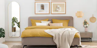 Beiges Polsterbett mit gelber Bettwäsche.