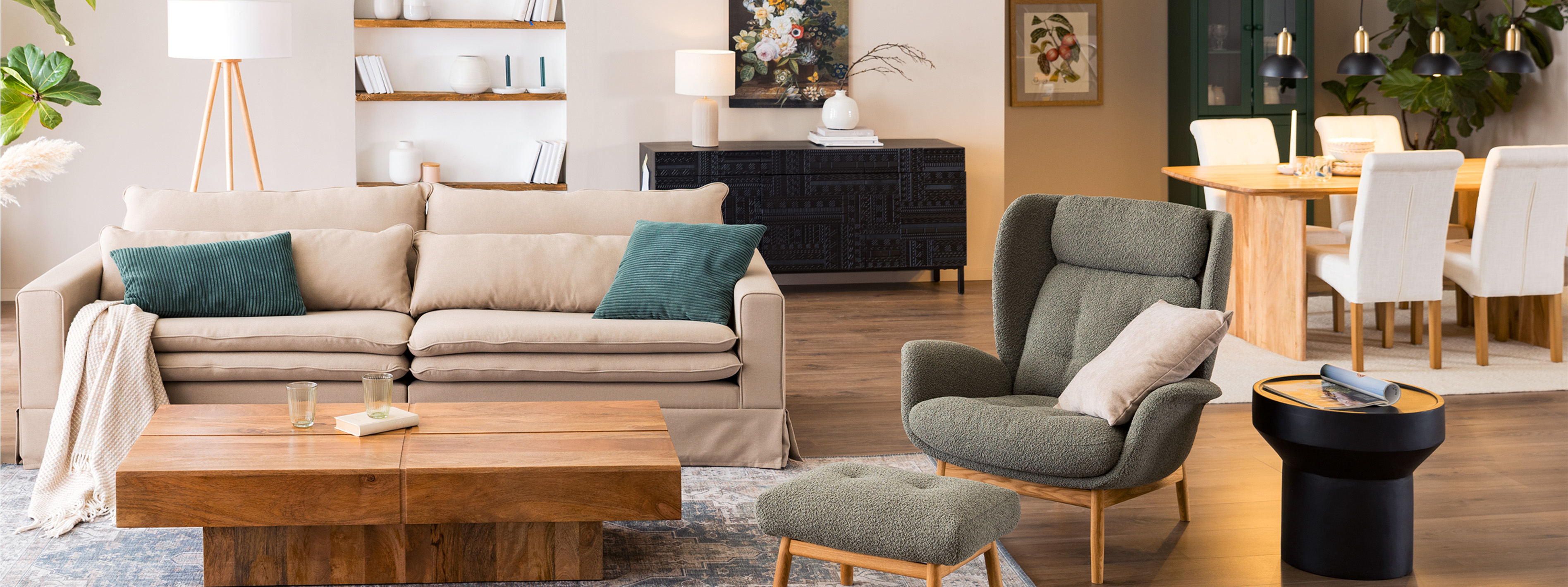 Offener Wohn- und Essbereich im britischen Landhausstil mit einem Couchtisch aus massivem Holz, einem beigen Sofa, einem moosgrünen Ohrensessel, vielen Textilien und einem stilvollen Tassenregal.