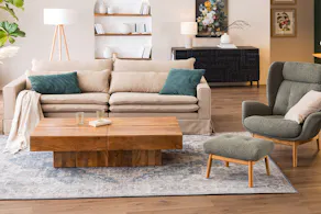 Espace salon et salle à manger ouvert au style maison de campagne britannique, avec une table basse en bois massif, un canapé beige, un fauteuil à oreilles vert mousse, de nombreux textiles et une étagère à tasses élégante.