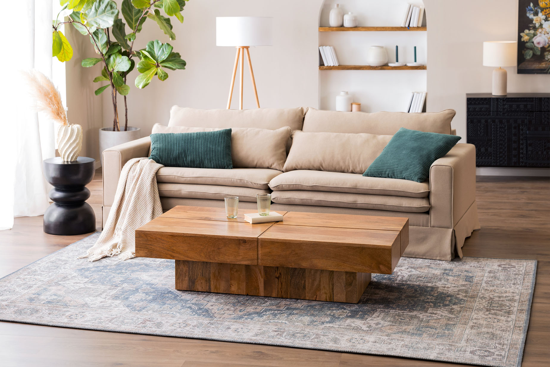 Espace salon et salle à manger ouvert au style maison de campagne britannique, avec une table basse en bois massif, un canapé beige, un fauteuil à oreilles vert mousse, de nombreux textiles et une étagère à tasses élégante.
