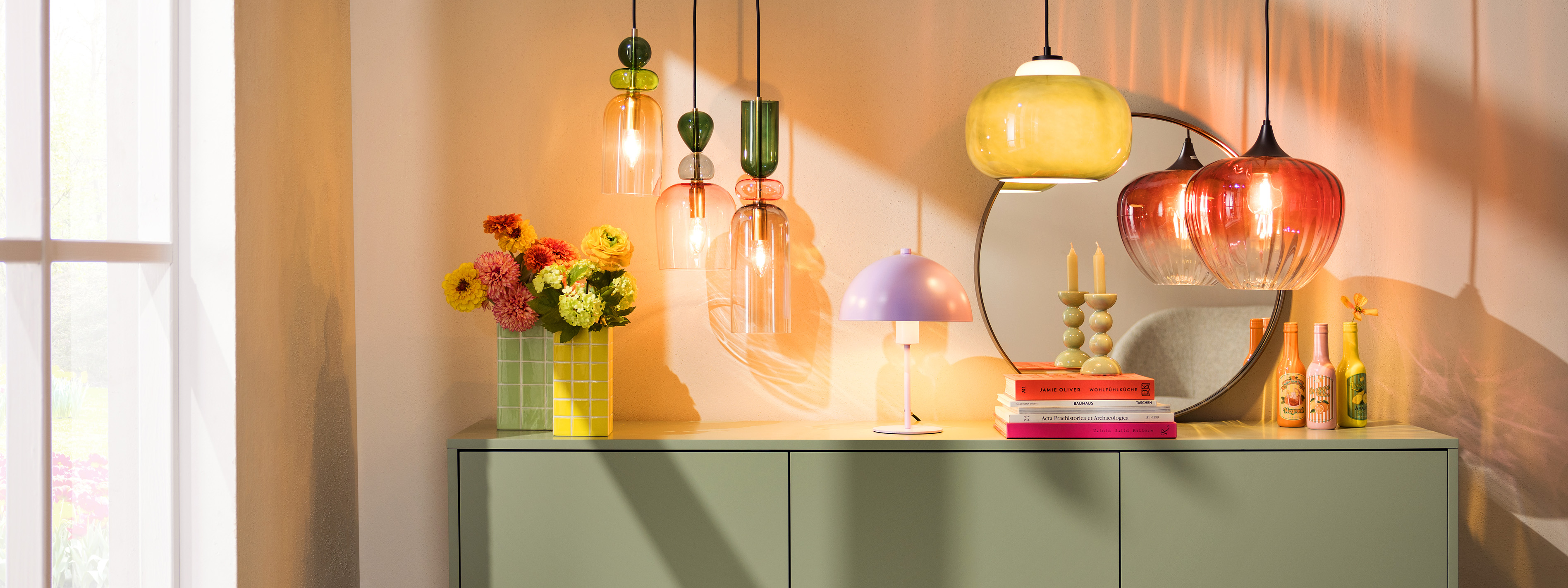 Fliederfarbene Mushroom-Tischleuchte auf einem Sideboard sowie weitere bunte Pendelleuchten im Retro-Stil.