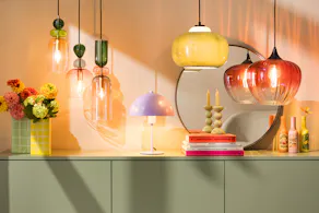 Lampe champignon couleur lilas sur un buffet, ainsi que d’autres suspensions colorées de style rétro.