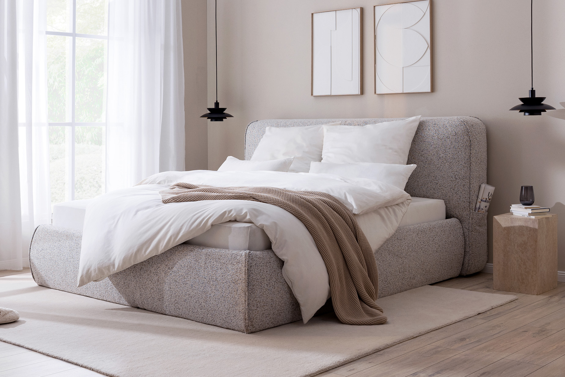 Chambre reposante dans des tons chauds de gris, de beige et de bois, avec un lit capitonné gris, un fauteuil gris foncé, du linge de lit assorti et un buffet en bois clair.