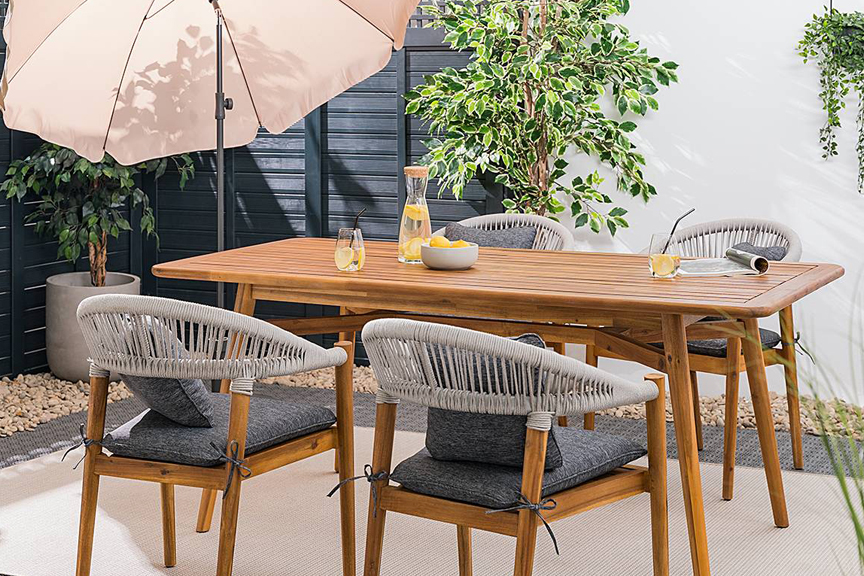 Moderne Terrasse mit einer Outdoorlounge aus Teakholz und Edelstahl von der BUTLERS-Möbelserie Teakline, dazu gemütliche Textilien wie Kissen und ein Outdoorteppich sowie weitere Gartenaccessoires.