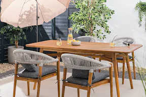 Moderne Terrasse mit einer Outdoorlounge aus Teakholz und Edelstahl von der BUTLERS-Möbelserie Teakline, dazu gemütliche Textilien wie Kissen und ein Outdoorteppich sowie weitere Gartenaccessoires.