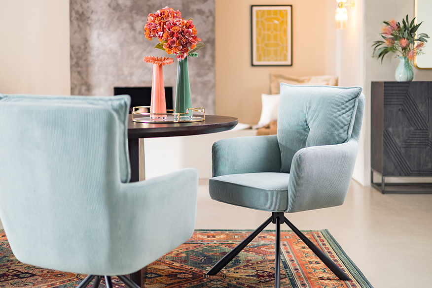 Zwei hellblaue Esszimmer-Armlehnenstühle aus bequemem Cord vor einem schwarzen, runden Esstisch, der mit Blumen dekoriert ist.