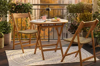 Gemütlicher Balkon mit Klappmöbeln aus massivem Holz und Seilgeflecht, dazu viele Balkonpflanzen und ein Outdoorteppich.