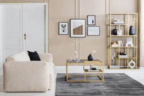 Wohnzimmer mit einem beigen Bouclésofa und -sessel; ein Couchtisch, Regal, TV-Board sowie eine Kommode in einer eleganten Schwarz-Gold-Kombination, dazu schwarze und weiße Deko und viele Textilien.