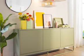 Grünes Sideboard mit bunter Deko und organisch geformtem Dekospiegel.
