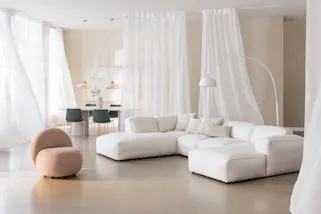 Espace salon et salle à manger de la couleur Pantone Clooud Dancer, avec de légers rideaux beiges et des meubles blancs