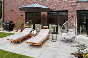 Belle terrasse avec transats beiges, parasol gris foncé et fauteuil suspendu, ainsi qu'une desserte.