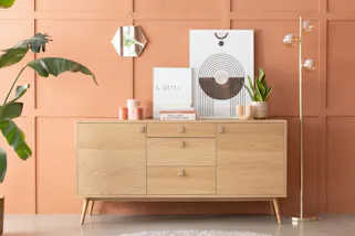 Verspielt dekoriertes Sideboard aus hellem Eichenholzfurnier vor einer orangen Akzentwand.