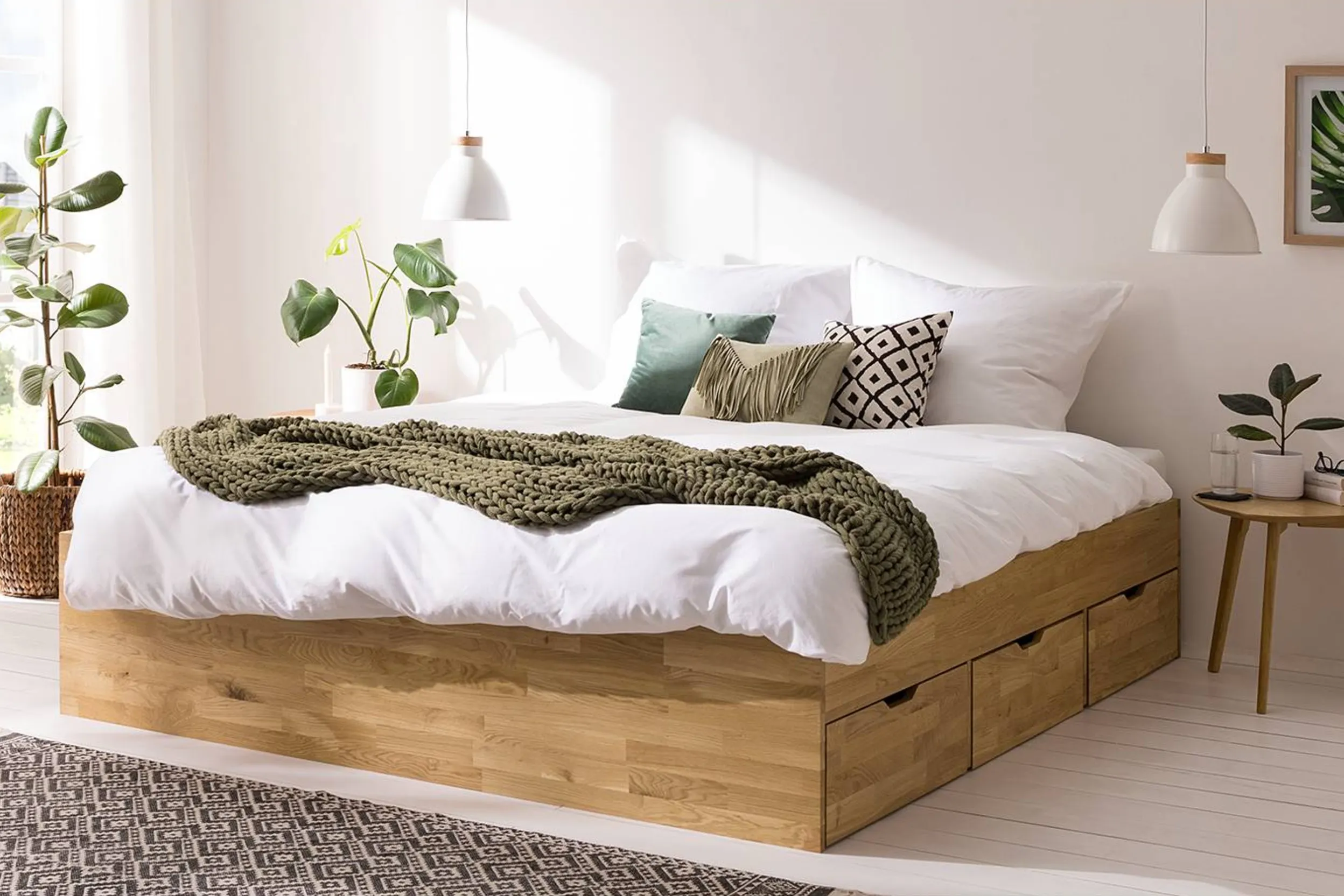 Schlafzimmer mit Pflanzen und massivem Schubladenbett samt weisser Bettwäsche