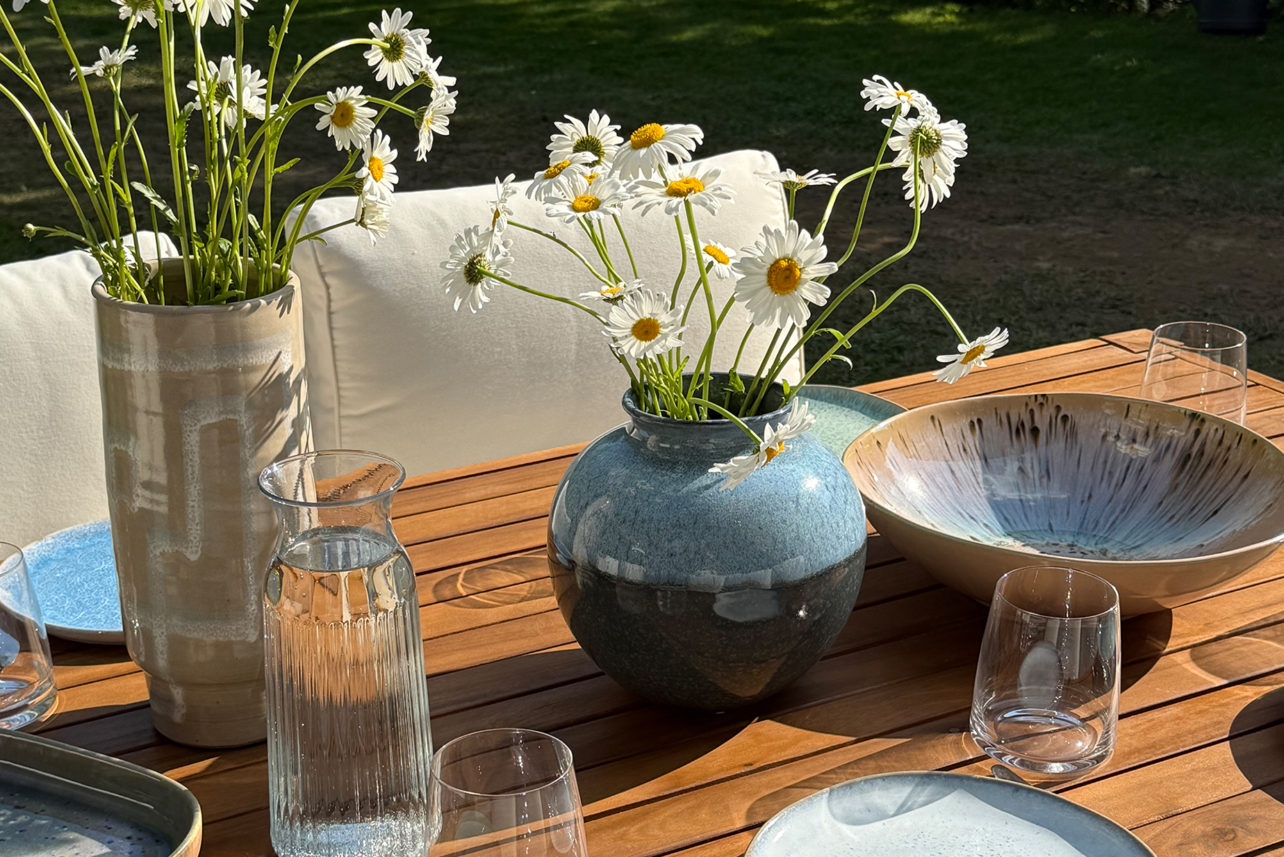 Gedeckter Gartentisch aus Akazienholz mit blauem Geschirr und schönen Blumen.