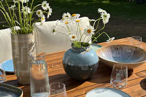 Gedeckter Gartentisch aus Akazienholz mit blauem Geschirr und schönen Blumen.