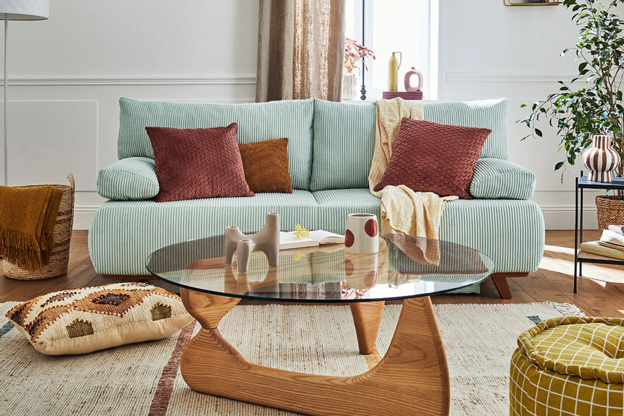Wohnzimmer mit türkisem Sofa, braunem Glas-Couchtisch und bunten Textilien