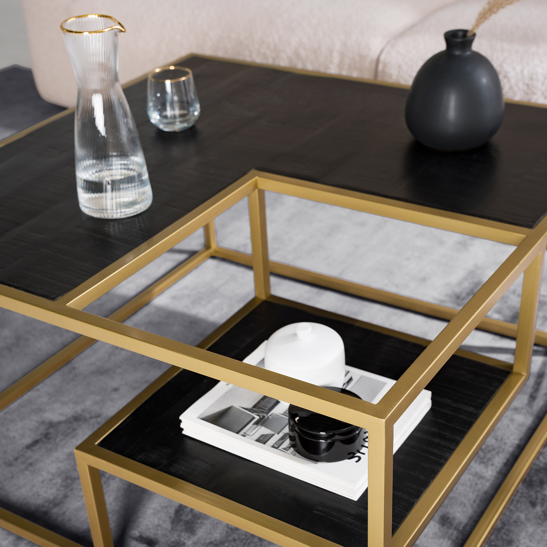 Table basse avec plateau noir et structure en métal doré sur un tapis gris, objets décoratifs noirs et balncs