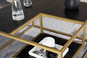Table basse avec plateau noir et structure en métal doré sur un tapis gris, objets décoratifs noirs et balncs