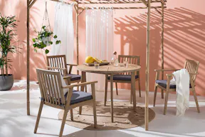 Gartenstühle und Gartentisch aus Holz mit Juteteppich, Leinen und Grünpflanzen im Boho-Look.