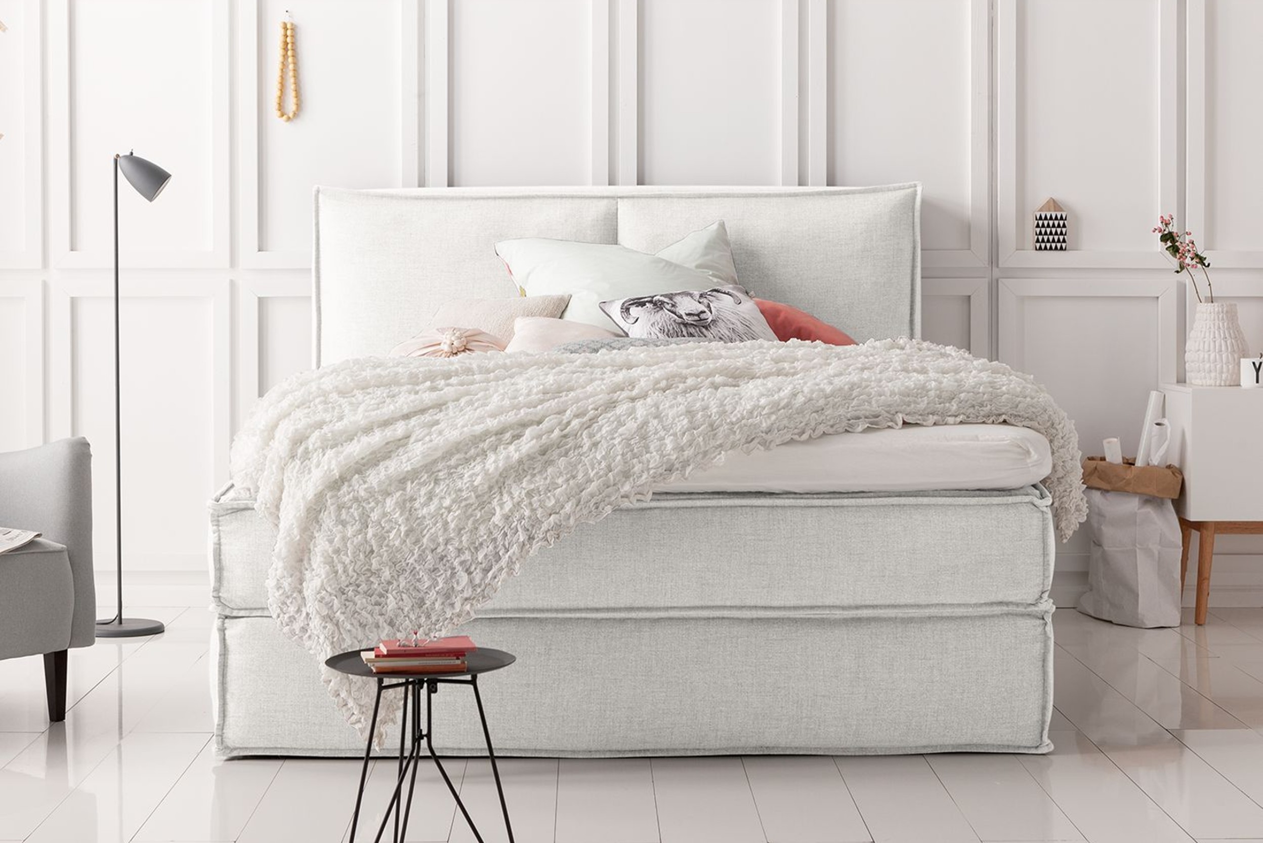 Weißes Boxspringbett mit kuscheliger Tagesdecke vor weißer Wand