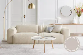 In Weiß und Cremetönen gehaltenes Altbau-Wohnzimmer mit goldener Steh- und Pendelleuchte, beigem Teppich und mittig platziert einem mit Bouclé-Stoff bezogenen beigen Hocker und Sofa; daneben Detailbild von hellem Bouclé-Polsterbezug.