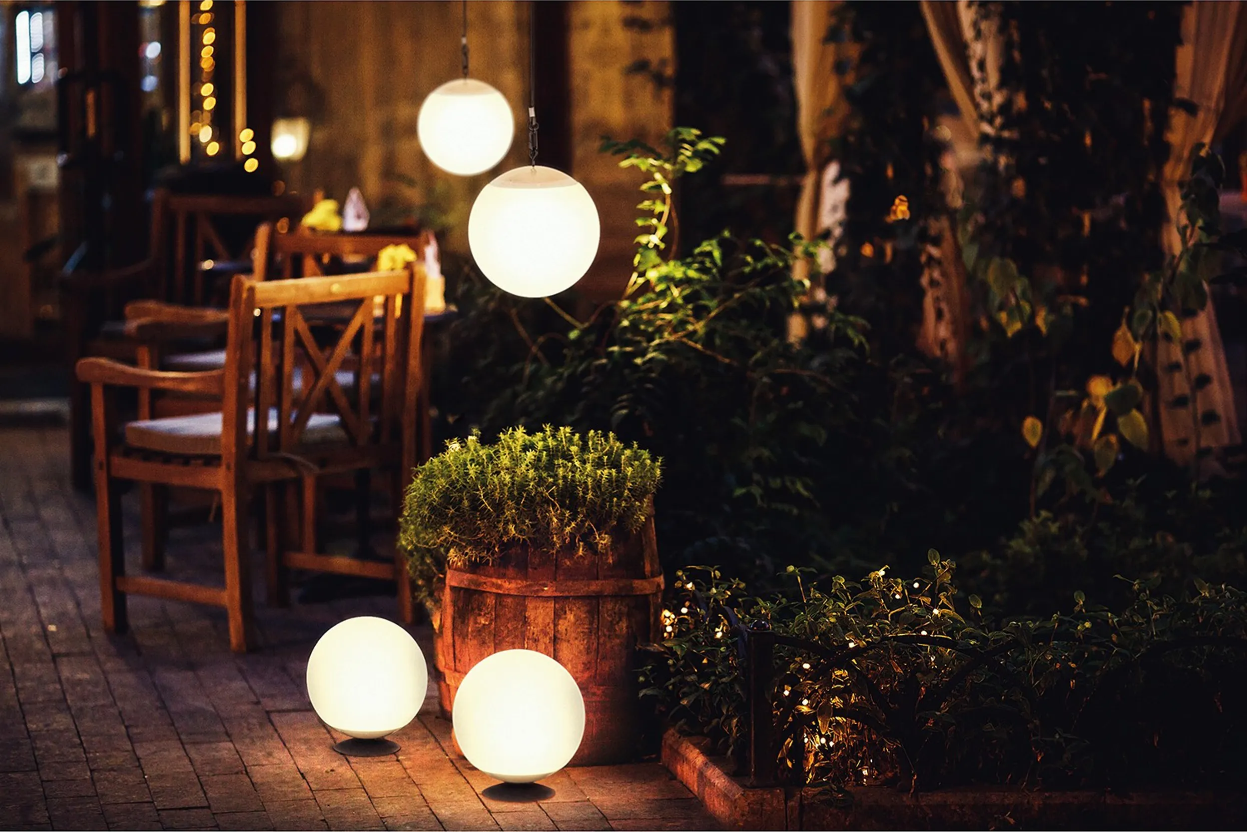 Terrasse mit Holzmöbeln und -accessoires sowie runden Pendel- und Dekorationsleuchten