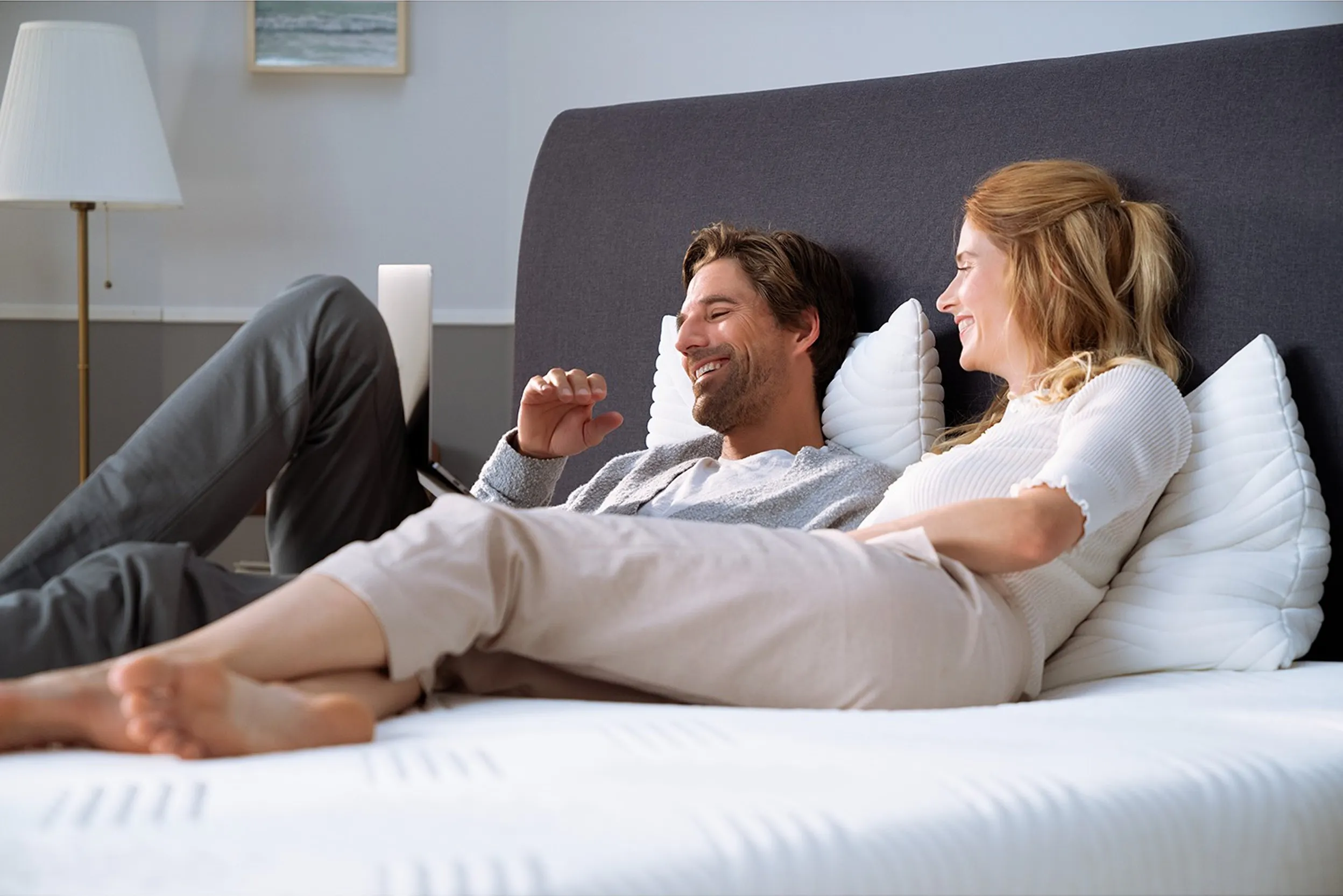 Lachendes Paar auf einer unbedeckten Matratze auf einem gepolsterten Bett mit einem großen Kopfteil